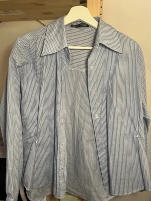 Blårandig skjorta - Klassisk blårandig skjorta med vit knappstängning och bred krage. Skjortan har lång ärm och är tillverkad i ett mjukt bomullsmaterial. Perfekt för en avslappnad men ändå stilren look.