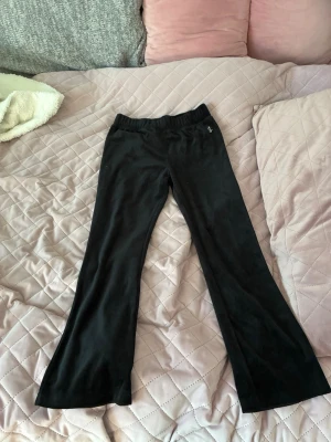Svarta mjukisbyxor från Juicy Couture - Säljer ett par svarta mjukisbyxor från Juicy Couture med JC-logga vid höften. Byxorna har bootcut-modell, resår i midjan och är gjorda i mjuk sammet som känns riktigt skön mot huden. Perfekta för chill dagar eller när du vill ha en avslappnad look.