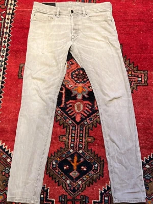Ljusgrå Diesel jeans straight fit - Säljer ett par ljusgrå jeans från Diesel med klassisk femficksmodell och raka ben. Jeansen har diskreta sömmar, normal passform och är tillverkade i mjuk bomullsdenim. Perfekta för dig som gillar stilrena och enkla jeans.