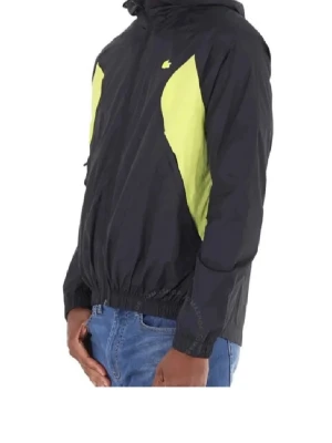 Svart och gul vindjacka från Lacoste - Snygg svart vindjacka från Lacoste med gula detaljer på sidorna. Jackan har huva, elastisk midja och är tillverkad i lätt syntetmaterial. 