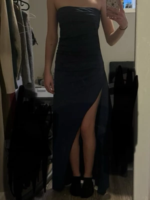 Marinblå balklänning - Säljer en marinblå långklänning med omlottdetalj och draperad effekt upptill. Klänningen är axelbandslös, funkar super bra till balklänning tex. den är aldrig använd bara testad och sitter fint, vet tyvärr inte vart den är ifrån. men fof fin med mjukt material. 