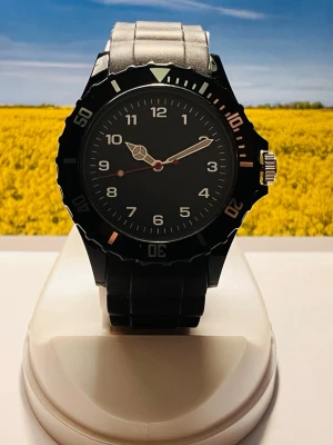 Svart sportig  klocka - Stilren svart analog klocka med rund urtavla och tydliga vita siffror. Klockan har en vridbar bezel med vita markeringar och ett robust svart silikonarmband. Perfekt för dig som gillar en enkel men sportig look. Rustad med nytt batteri, säljes i befintligt skick enligt bilderna!