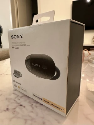 Sony WF-1000X trådlösa in-ear hörlurar - Snygga svarta trådlösa in-ear hörlurar från Sony, modell WF-1000X. Kommer med laddningsetui och extra öronproppar i olika storlekar. Hörlurarna har aktiv brusreducering och Bluetooth, perfekt för musik och poddar på språng.