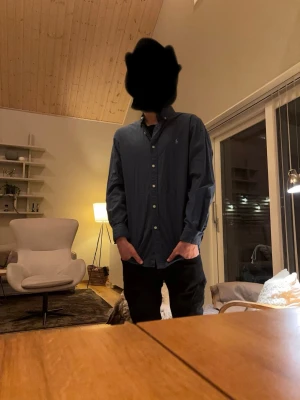 Blå skjorta från Polo Ralph Lauren - Klassisk blå skjorta från Polo Ralph Lauren med knappar framtill och broderad logga på bröstet. Skjortan har lång ärm och normal passform, perfekt för en stilren look. Tillverkad i mjuk bomull.