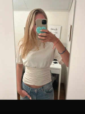 Vit croppad topp med snörning - Snygg vit croppad topp med korta ärmar och snörning i midjan som ger en tight passform. Perfekt till jeans eller kjol för en trendig look. Enkel och stilren design som passar till många outfits. Små defekter här och där, därav priset. 