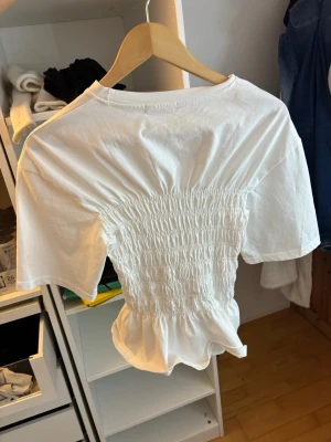 Vit smockad topp med volang - Superfin vit topp med smockad midja och volang nertill från Missäy. Säljer för att jag aldrig använder den, helt oanvänd och den är i storlek S/M men jag brukar ha XS och den passar mig perfekt ❤️