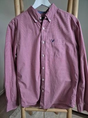 Rutig skjorta American Eagle, storlek M - Snygg rödvitrutig skjorta från American Eagle med klassisk passform. Skjortan har knappar hela vägen, bröstficka med logga och button-down krage. 100 % bomull, storlek M.