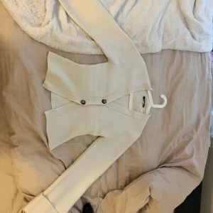 Krämvit cardigan från Gina tricot - Snygg krämvit kofta med två stora bruna knappar framtill. Koftan har v-ringning, lång ärm och lätt figursydd passform. Använd kanske 2 gånger.