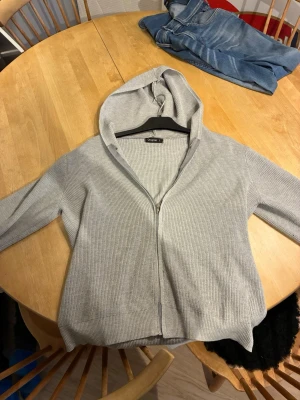Grå zip riktigt skön  - Säljer en stilren grå hoodie i ribbat material. Hoodien har dragkedja framtill, luva och långa ärmar. Perfekt för en avslappnad och trendig look. Passar till jeans eller mjukisbyxor för en chill vibe.