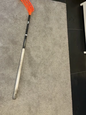 Unihoc innebandyklubba svart/orange - Säljer en Unihoc innebandyklubba med svart skaft och orange blad. Skaftet är märkt med 'CARBSKIN CLASSIC' och har vitt grepp. Perfekt för dig som gillar innebandy och vill ha en lätt och smidig klubba.
