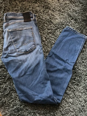 Blå jeans från Replay - Säljer ett par klassiska blå jeans från Replay med raka ben och snygga kontrastsömmar på bakfickan. Jeansen har en normal passform och är tillverkade i mjukt bomullsdenim. Perfekta för dig som gillar stilrena och tidlösa jeans.