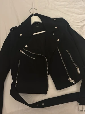 Svart skinnjacka från Pull&Bear - Snygg svart skinnjacka från Pull&Bear med flera silvriga dragkedjor,  och bälte i midjan som sitter fast så den åker inte av. Den är super bra skick och har inga tecken på användning, priset kan diskuteras.💕💕