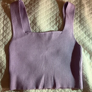 Ljuslila ribbad linnetopp - Säljer en ljuslila ribbad linnetopp med breda axelband och fyrkantig halsringning. Toppen är croppad och har en enkel, stilren design som passar perfekt till jeans eller kjol. Materialet är mjukt och stretchigt för en bekväm passform! :)