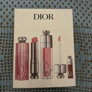 Dior Addict Lip Glow Kit - Lyxigt kit från Dior med tre läpprodukter: ett rosa Lip Glow Color Reviver Balm, ett nude läppglans och ett miniläppglans i brunrosa nyans. Snygga förpackningar i silver och transparent plast med Dior-logga. Perfekt för dig som älskar glansiga och återfuktade läppar.