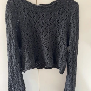Svart stickad tröja från Monki - Säljer en svart stickad tröja från Monki i storlek S. Tröjan har ett snyggt hålmönster, lång ärm och en lite croppad passform. Perfekt att styla med höga jeans eller kjol för en trendig look.