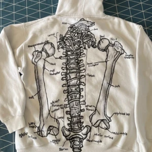 Vit hoodie med anatomiskt tryck - Vit hoodie med svart anatomiskt tryck på ryggen som visar ryggrad och ben, samt text och handmotiv framtill. Mjuk och skön, perfekt för dig som gillar unika och konstnärliga plagg. #Handgjord
