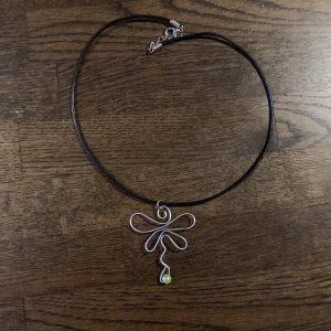 Halsband med en trollslända och grön pärla - Unikt halsband med svart snöre och ett handgjort hänge i silverfärgad metalltråd (som dock kommer att bli svart och missfärgad på baksidan vid användning), format som en trollslända med en liten grön pärla längst ner. Perfekt för dig som gillar personliga och kreativa accessoarer.