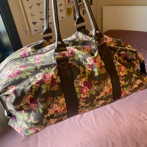 Blommig dufflebag - Fräsch söt blommig dufflebag som endast har använts cirka två gånger. Väskan har bruna handtag och axelrem, samt dragkedja upptill. Passar bra för resor eller övernattningar💕