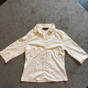 Vit skjorta från KappAhl, strl 42 - Klassisk vit skjorta från KappAhl i storlek 42. Skjortan har trekvartsärm, krage och knäppning framtill. Perfekt till jeans eller kjol för en clean och enkel look. Tillverkad i mjukt bomullstyg som känns skönt mot huden.