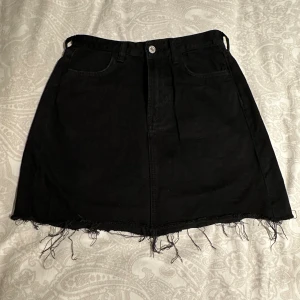 Svart jeanskjol från H&M &Denim - Svart jeanskjol från H&M &Denim i klassisk femficksmodell med framsig fåll.