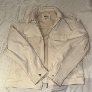 Beige overshirt från Bershka - Snygg beige overshirt från Bershka med klassisk krage, två bröstfickor och dragkedja framtill. Jackan har lång ärm och är tillverkad i ett mjukt material med lätt struktur. Perfekt för lager-på-lager och stilrena outfits.