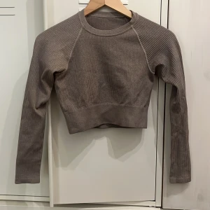 Ribbad croppad träningströja - Snygg croppad brun tröja med ribbad struktur och lång ärm. Tillverkad i Italien av polyamid, polyester och elastan för en skön stretchig passform. Diskret logga på ryggen. Knappt använd.