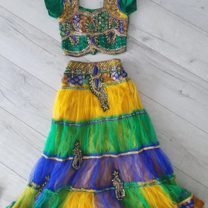Färgglad barn långklänning med broderi - Säljer en( barn storlek 7-8år)maxad långklänning i grönt, gult och blått med glittriga detaljer och broderier. Toppen har korta ärmar, snörning i ryggen och coola pärlbroderier framtill. Kjolen är i lager på lager med mesh och har dragkedja i sidan.