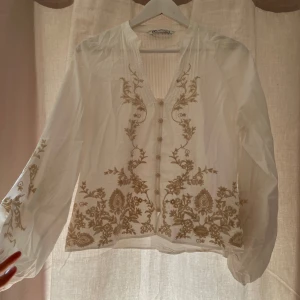 Vit broderad blus från Zara - INTRESSEKOLL! Säljer en superfin vit blus från Zara med beige broderade detaljer och knappar framtill. Blusen har långärmade, lite puffiga ärmar och v-ringning.💗