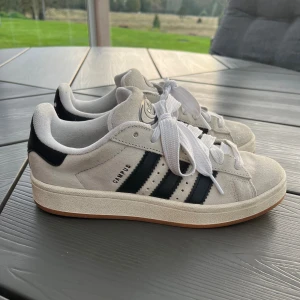 Adidas Campus 00s beige  - Säljer ett par Adidas Campus 00s i beige mocka med svarta ränder och vit sula. Skorna kommer inte till användning längre men är i bra skick. Några märken vid tån som syns på sista bilden men inget man tänker på. Finns även svarta skosnören till. Nypris 1345kr. 