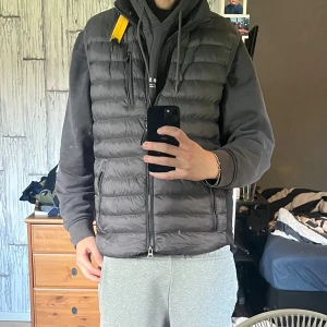 Grå dunväst från Parajumpers - Säljer en grå dunväst från Parajumpers. Västen har dragkedja framtill, flera fickor och snyggt broderat PJS-märke i nacken. Perfekt att slänga över en hoodie för en chill look. Köpt förra veckan använd 4 gånger.