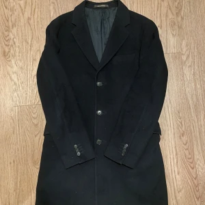 Marinblå Kashmir rock från Oscar Jacobson - Klassisk marinblå rock från Oscar Jacobson med tre knappar framtill, krage med slag och fickor med lock. Jackan är helfodrad och har en stilren, rak passform. Perfekt för dig som vill ha en tidlös och snygg look under höst och vinter. Med Kashmir.