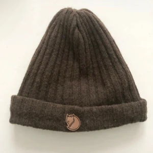  Fjällräven mössa grön  - Snygg grön ribbstickad mössa från Fjällräven med uppvikt kant och klassisk rävlogga framtill. Tillverkad i mjuk ull som håller dig varm. Liten svensk flagga på baksidan ger extra stilpoäng. Perfekt för kalla dagar.Storlek 54/58 CM Färg:Grön ordpris:699 kr Bilderna togs personligen av mig, vilket säkerställer att du ser exakt den produkt du köper. Vänligen observera att jag inte har öppetköp.Skickar endast med PostNord.