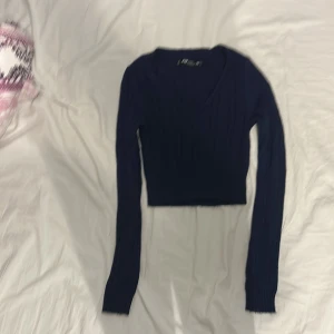 Mörkblå croppad stickad tröja XS - Mörkblå croppad stickad tröja från FB Sister i storlek XS. Tröjan har v-ringning, ribbade muddar och lång ärm. Snyggt ribbat mönster som ger en trendig look och passar perfekt till höst och vinter.