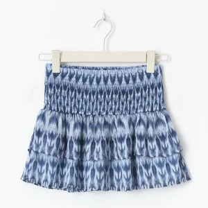 Blå mönstrad kortkjol med volang - Supersöt kortkjol i blått med ett unikt mönster och smockad midja. Kjolen har volangdetaljer och är tillverkad i ett lätt och luftigt material som passar perfekt för varmare dagar. Perfekt att styla med en enkel topp och sneakers.