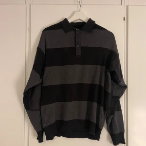 Randig pikétröja från Ted Lapidus - Snygg pikétröja från Ted Lapidus i storlek M. Tröjan har breda svarta och gråa ränder, klassisk krage och knäppning med två knappar. Materialet är mjukt och stickat, perfekt för dig som gillar en chill och stilren look.