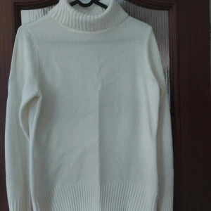 Vit polotröja med ribbade detaljer - Klassisk vit polotröja med hög krage och ribbade muddar vid ärmslut och nederkant. Tröjan är stickad och har en enkel, stilren design som passar perfekt till kyligare dagar. Mjuk och skön känsla, lätt att matcha med olika outfits.