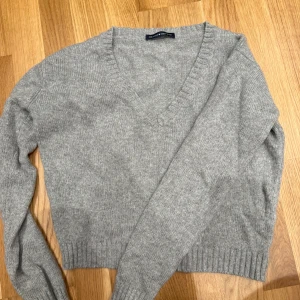 Grå stickad v-ringad tröja Brandy Melville - Mysig grå stickad tröja från Brandy Melville med v-ringning och långa ärmar. Tröjan har ribbade muddar vid ärmslut och nederkant, perfekt för lager på lager. Enkel och stilren design som funkar till allt.