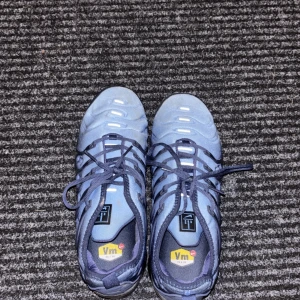 Nike Air Vapormax blå sneakers - Nike Air Vapormax sneakers i blått med svarta detaljer och genomskinlig, bubblig sula. Ovandel i syntetmaterial och textil, snörning framtill och rund tå. Snygg sportig look med ikonisk Vapormax-dämpning för extra komfort.