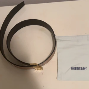 Burberry bälte med guldspänne - Snyggt Burberry bälte i klassiskt rutigt mönster med beige, bruna och röda toner. Bältet har ett exklusivt guldigt TB-spänne och är tillverkat i skinn. Perfekt accessoar för att lyfta din outfit med en lyxig touch. Köpt från farfetch kvitto finns, originalpris 5044kr