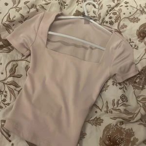 Ljusrosa topp med fyrkantig ringning Amisu - Supersöt ljusrosa topp från Amisu med korta ärmar och snygg fyrkantig ringning. Modellen är tight och croppad, perfekt till jeans eller kjol. Mjuk och stretchig i materialet, passar dig som gillar en enkel men trendig look.