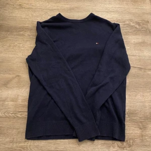 Mörkblå stickad tröja Tommy Hilfiger - Mörkblå stickad tröja från Tommy Hilfiger i pima bomull och kashmir. Klassisk modell med rund hals och liten broderad logga på bröstet. Långärmad och mjuk, perfekt för lager-på-lager under kyliga dagar. Kan säljas billigare ifall man köper mer från mig kan även sälja billigare annars!!?