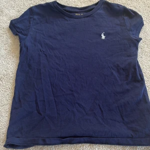 Marinblå t-shirt från Polo Ralph Lauren - Snygg marinblå t-shirt från Polo Ralph Lauren med klassisk vit broderad logga på bröstet. T-shirten har rund halsringning och korta ärmar. Tillverkad i mjuk bomull som är skön mot huden. Perfekt för en clean och stilren look.