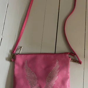 Rosa väska med vingar - Jättesöt, två stenar har åkt bort, lite färg är bortskavd från hörnen men annars är den fin🩷