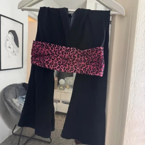Yoga pants med rosa leopardmönster - Coola svarta yoga pants med bred midjeresår i rosa leopardmönster. Byxorna har en rak och enkel form som ger en avslappnad vibe. Perfekt för dig som vill sticka ut med en färgglad detalj i outfiten.