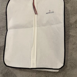 Blå Moncler dunjacka med huva - Säljer en blå dunjacka från Moncler med huva och dragkedja. Jackan har två snedställda fickor med dragkedja, en ärmficka med Moncler-logga och quiltad design. Materialet är polyester och dun, perfekt för kalla dagar. Snygg och sportig look. Storlek 12 år 152 cm