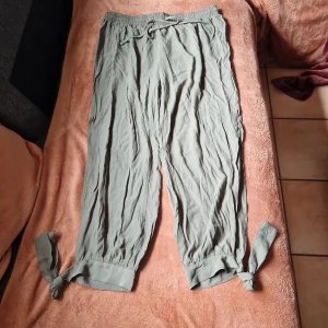 Ljusgröna byxor med knyt vid foten  - Snygga gröna byxor i 100% polyester med resår och snörning i midjan. Byxorna har breda ben och coola knytband vid bensluten för en avslappnad vibe. Perfekta för varmare dagar när du vill ha något luftigt och bekvämt. Midja ca cm 88 - 112.