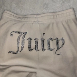 Krämvita Juicy Couture mjukisbyxor - Supermjuka krämvita mjukisbyxor från Juicy Couture med glittrande strassdetaljer och texten 'Juicy' på baksidan. Tighta i låren men raka ben. Minns inte exakt vilken affär men de är köpta i London