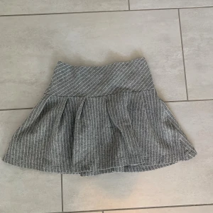 Grå kortkjol med ränder från Zara - Superfin grå kortkjol från Zara med vita tunna ränder. Kjolen har en markerad midja och veckad nederdel som ger en snygg volym. 