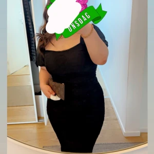 Svart figurnära klänning - Snygg svart klänning med figurnära passform och kort ärm. Klänningen har en smickrande v-ringning och markerad midja som framhäver siluetten. Perfekt för dig som gillar en stilren och klassisk look.