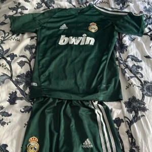 Real Madrid Ronaldo #7 grön matchtröja - Säljer en grön Real Madrid fotbollströja från Adidas med Ronaldo och nummer 7 på ryggen. Tröjan har korta ärmar, vita detaljer och klubbmärke på bröstet. Materialet är lätt och andas, perfekt för träning eller match. Bwin-logga på framsidan och klassiska Adidas-ränder på axlarna. För Barn 